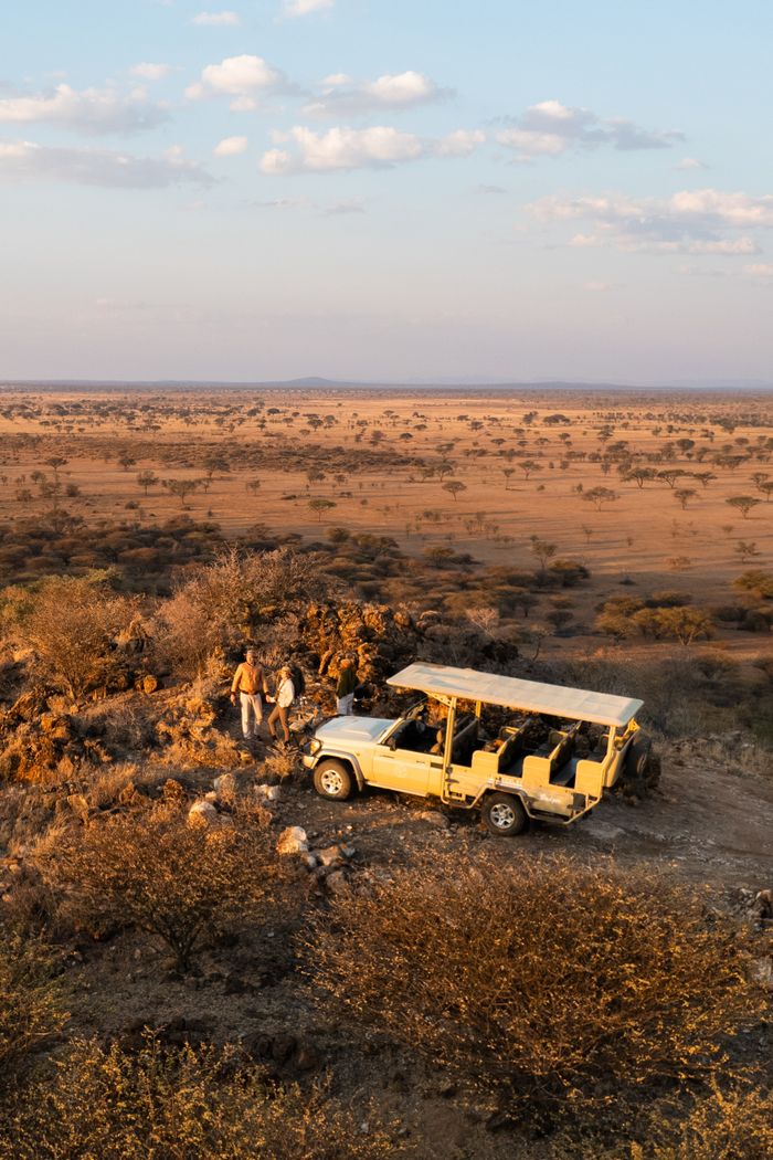 A safari jeep with two people in the African Savannah at sunset.