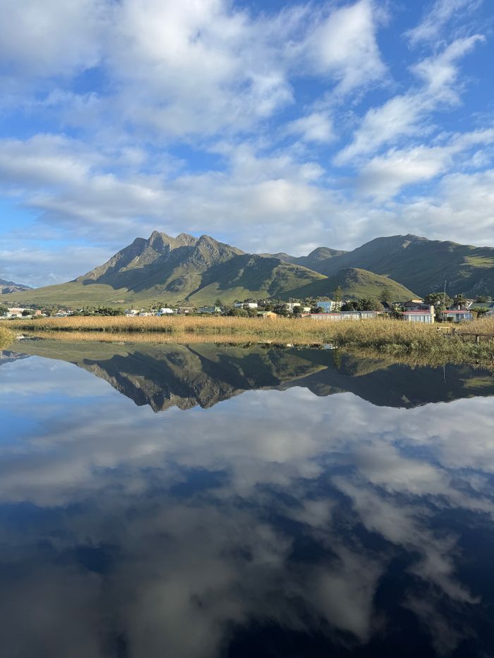 Beautiful reflection of green mountains in still water under a blue sky in South Africa, with a small town nearby.